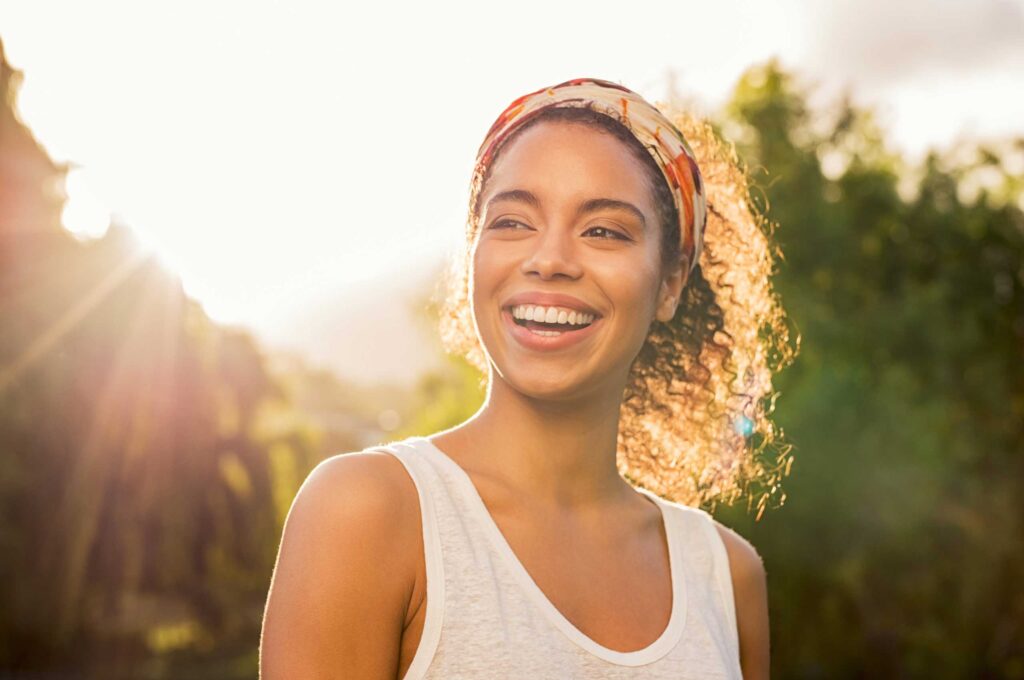Woman outside smiling in the sunlight, symbolizing the bright and healthy smiles created at Schlueter Periodontics.