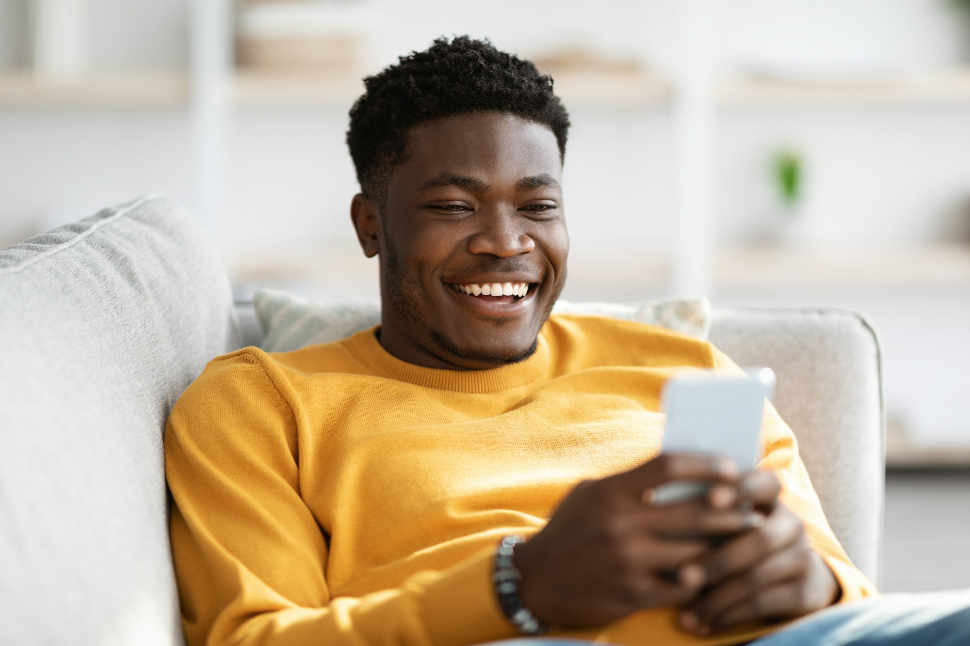 Smiling man reclining on a couch with a cellphone, depicting the relaxed post-care of Pocket Reduction surgery at Schlueter Periodontics.