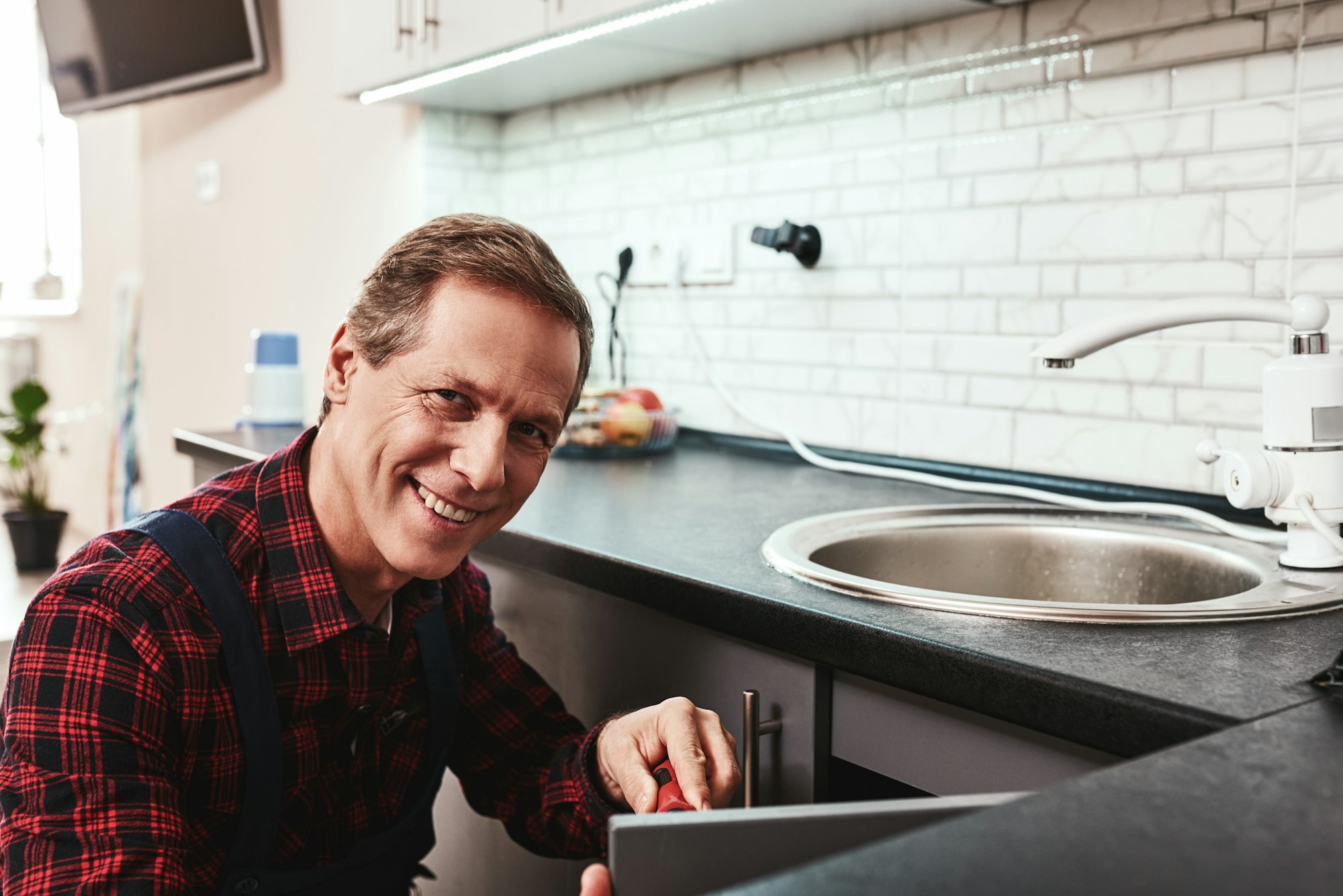 Handyman repairing a sink and smiling, metaphor for the restorative and reliable LANAP gum treatment at Schlueter Periodontics.