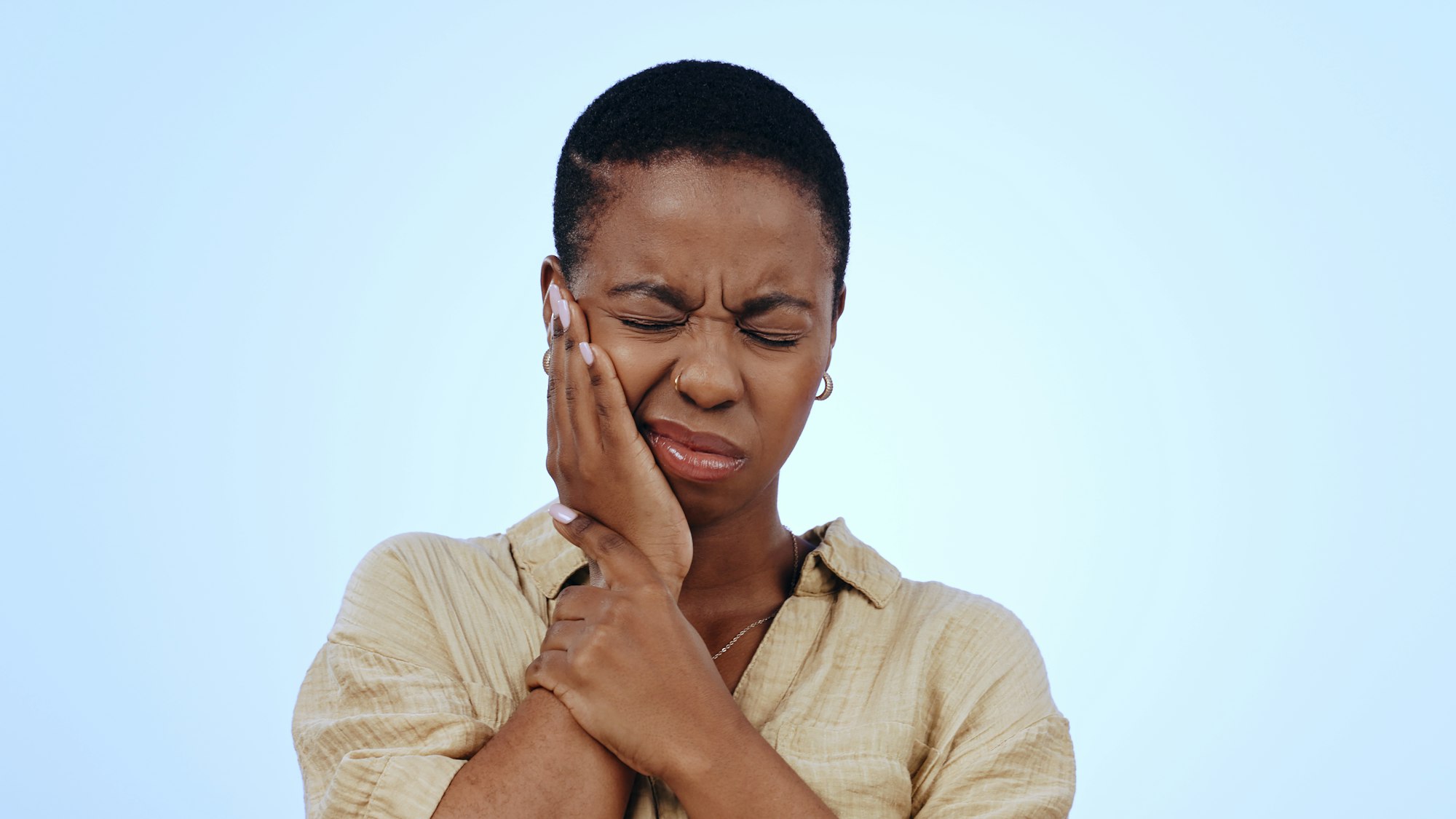 African American woman rubbing her jaw in pain, illustrating the discomfort of Swollen Gums treated at Schlueter Periodontics.