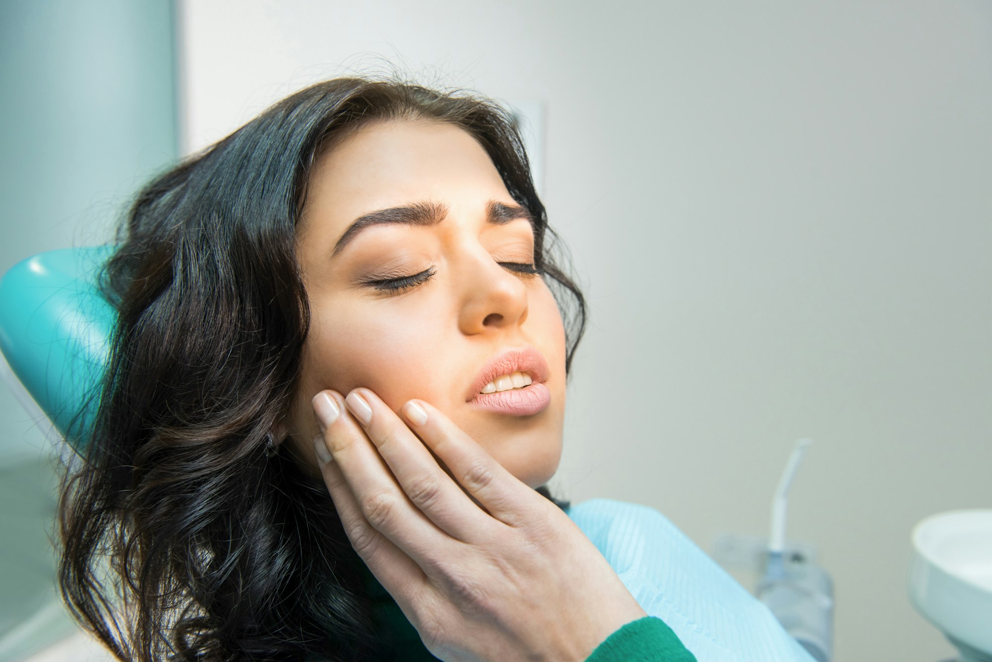 Young woman rubbing her jaw while in a dental chair, showing the pain associated with Gum Disease treated at Schlueter Periodontics.